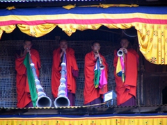 Blowing on the long horns atop the roof of the Paro Tsechu building