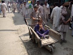 A boy being pushed in a cart whistles loudly as we take a photo of a typical Dir bazaar scene