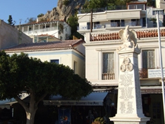A small monument stands in the shadow of the clock tower; Poros Town