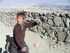 A boy playing ball runs alongside our vehicle; Kabul