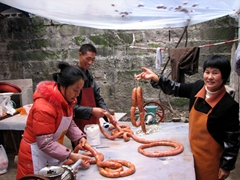 A proud Chinese lady holds up a freshly wrapped sausage for inspection
