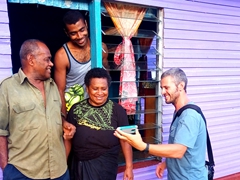 Robby showing the village chief and his wife their photo whle Manasa smiles in amusement; Tabia Village